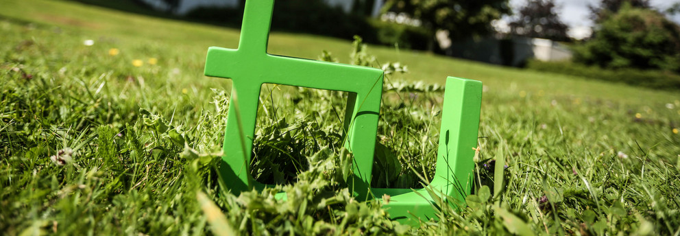 TU-Logo Im Vordergrund steht das TU-Logo im Gras, im Hintergrund das Audimax.